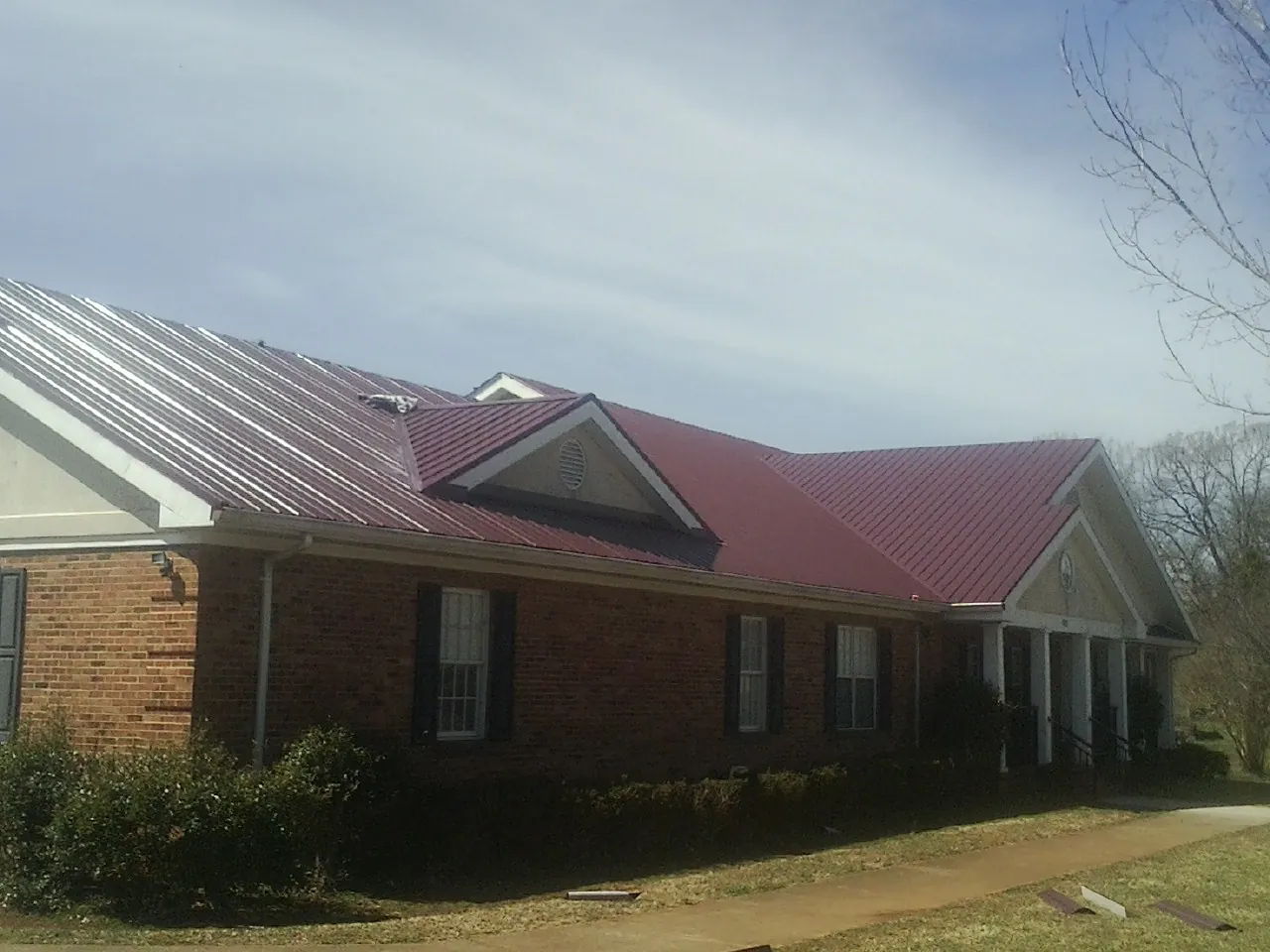 Red metal roof with gabled entries on a long brick building, from a Hail Damage Roof Repair job in Connoquenessing