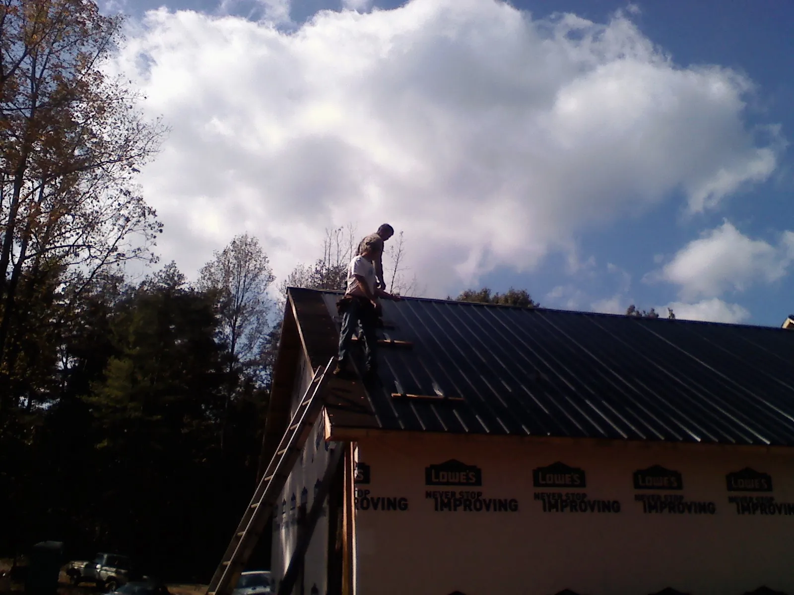 Roofer fastening dark metal panels high against a cloudy sky, from a Roof Inspection job in Connoquenessing