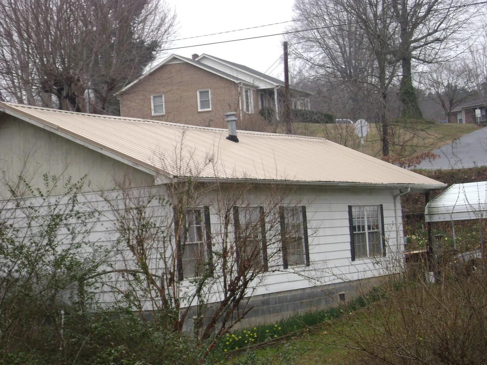 Tan metal roof on a white sided house set into a hillside — Commercial Roofing by Roofing Brothers in Connoquenessing
